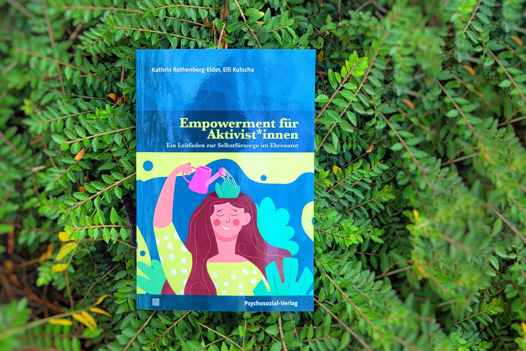 In einem grünen Busch liegt das Buch "Empowerment für Aktivist*innen" von Kathrin Rothenburg-Elder und Elli Kutscha